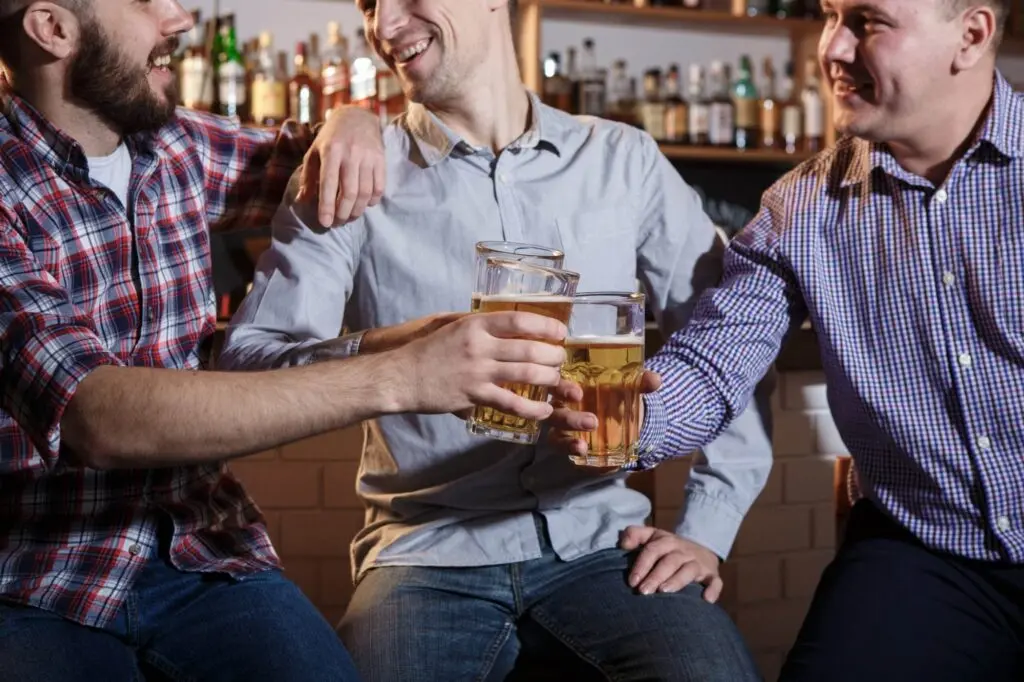 happy friends drinking beer at counter in pub
