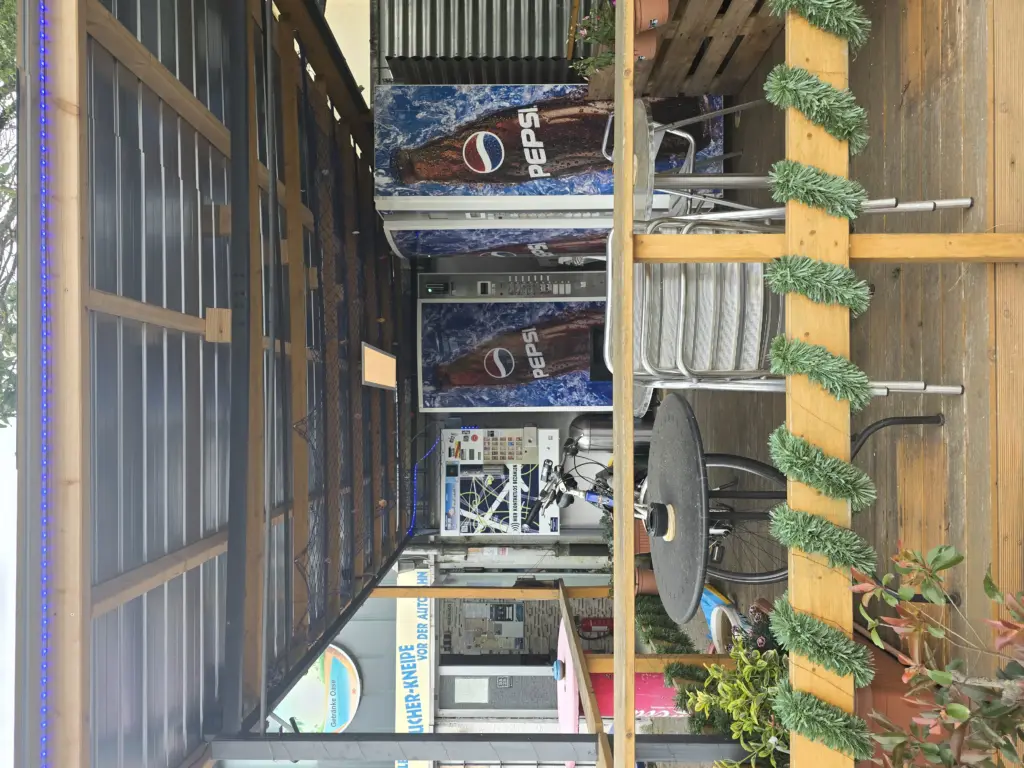 Sitzbereich im Freien mit Metallstühlen, einem runden Tisch und zwei Pepsi-Automaten im Hintergrund.