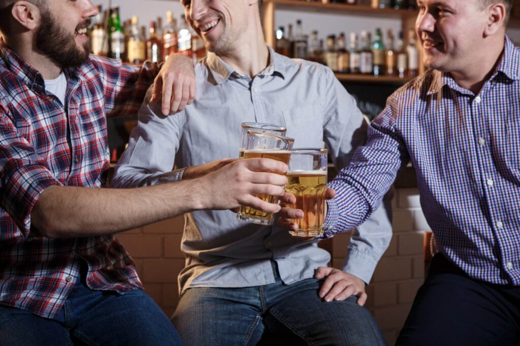 happy friends drinking beer at counter in pub