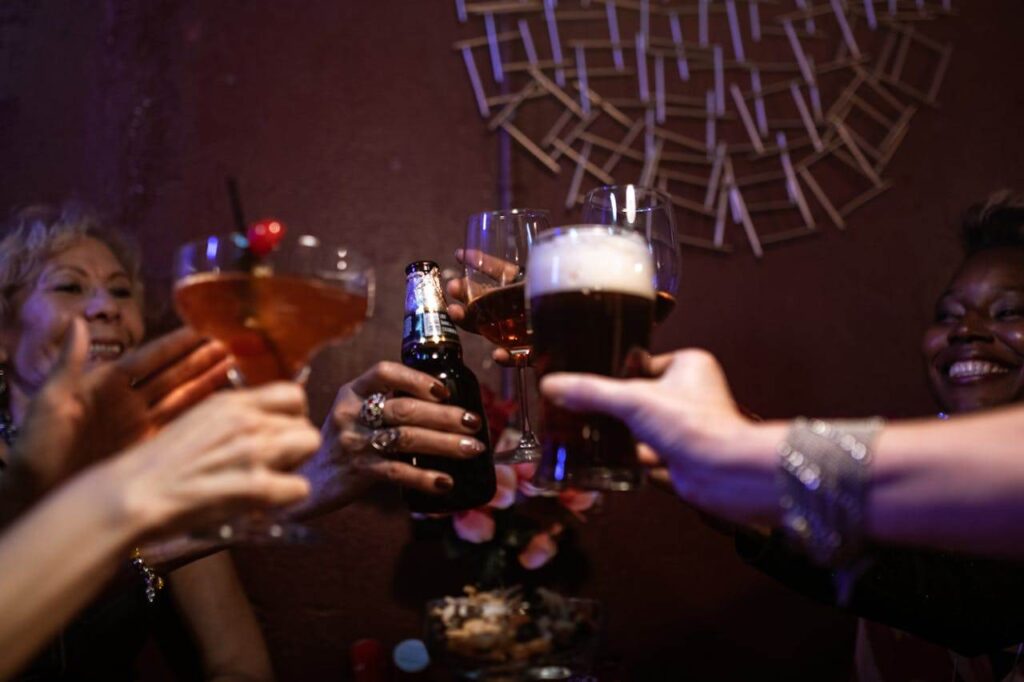 Gruppe von Menschen stößt mit Bier und Cocktails an, Blumen und Snacks auf dem Tisch.